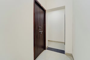 A hallway with a wooden door, a tiled floor, and a white wall.