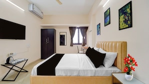 Quarto de hotel com cama, mesa de cabeceira, escrivaninha, tábua de passar roupa, televisão de tela plana e janela com cortinas.