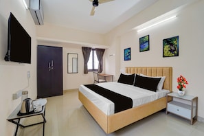 A hotel room with a bed, bedside table, a desk with a chair, a TV, and artwork on the walls. - Palette Legacy Apartment-Saravanampatti (Coimbatore)