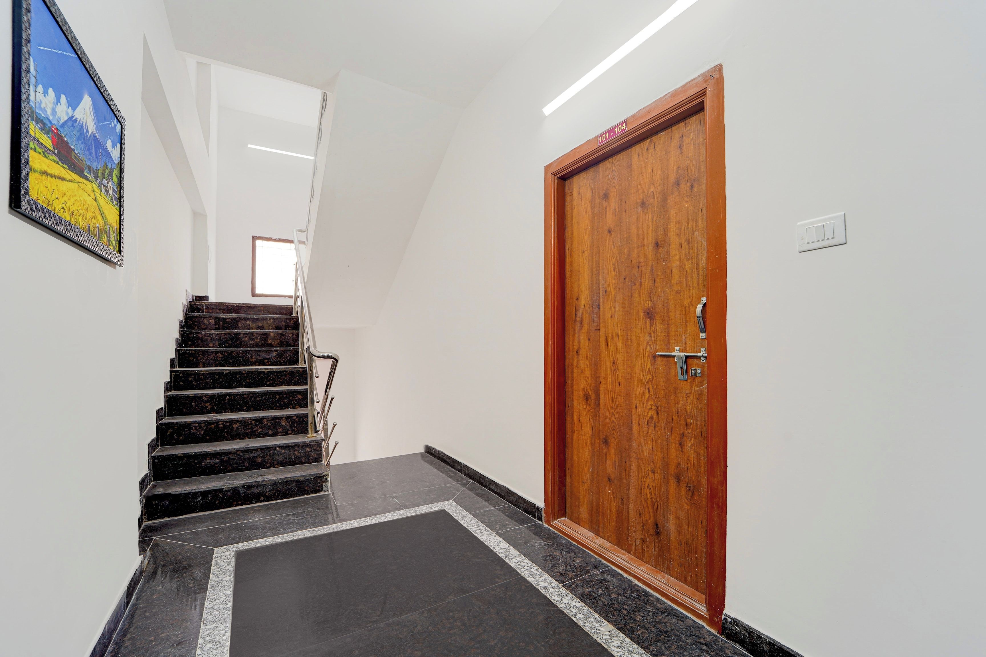 Un pasillo con una puerta de madera, una escalera y un cuadro en la pared.
