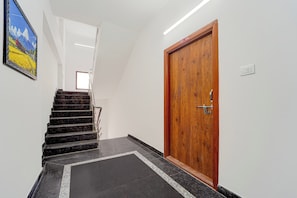 A hallway with a wooden door, a staircase, and a framed picture on the wall.