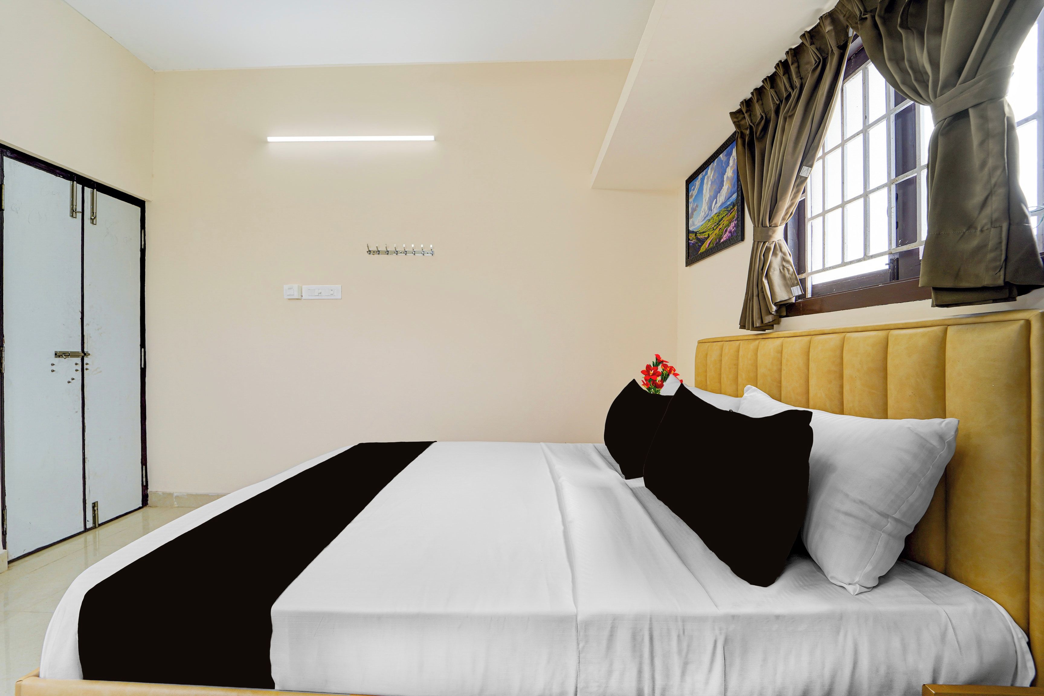 Una habitación de hotel con una cama, un armario, un cuadro y una ventana con cortinas.