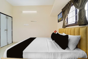 A hotel room with a bed, a wardrobe, a painting, and a window with curtains.