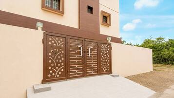 Un edificio moderno con fachada color beige, una puerta marrón con detalles decorativos y un pequeño ventanal encima de la puerta.