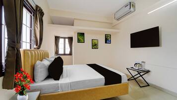 A hotel room with a bed, a small table with a kettle, a flat-screen TV, and artwork on the walls.