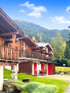A wooden chalet with a balcony, stone foundation, and a view of a forested mountain. - Chalet Apartment 5 Minutes Walk to Medran Lifts (Val de Bagnes)