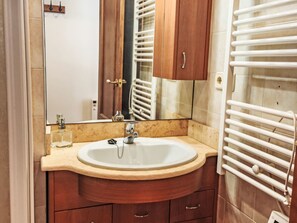 Een badkamer met een wastafel, spiegel, houten kastjes en een handdoekrek.