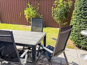 A patio with a table and chairs, a metal grill, and a wooden fence in the background. - Nordziel by Interhome (Norddeich)