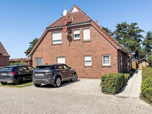 A two-story brick house with a sloped roof, a satellite dish, and a driveway with two parked cars. - Nordziel by Interhome (Norddeich)