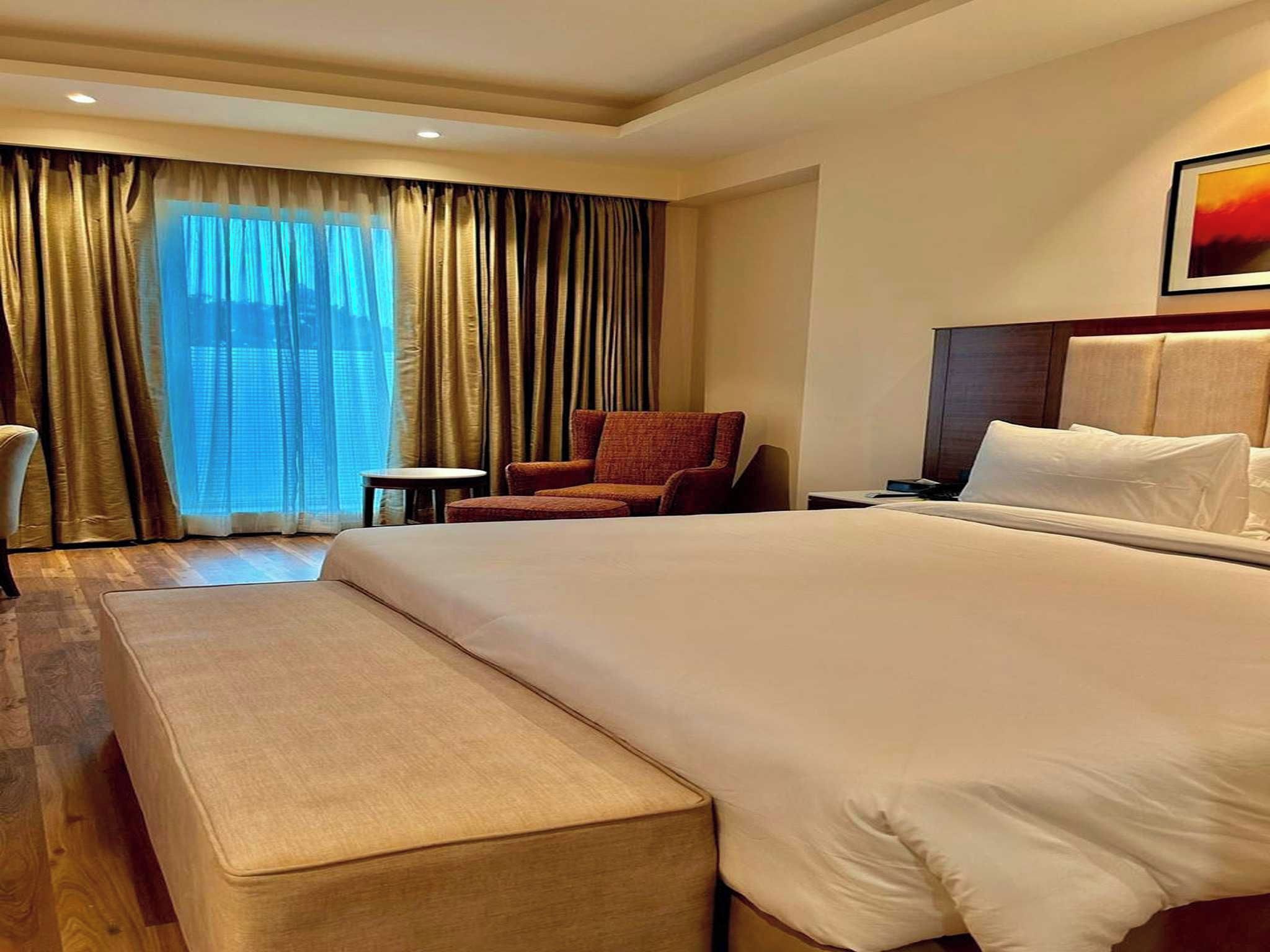 A hotel room with a large bed, a chair, a small table, and a nightstand.