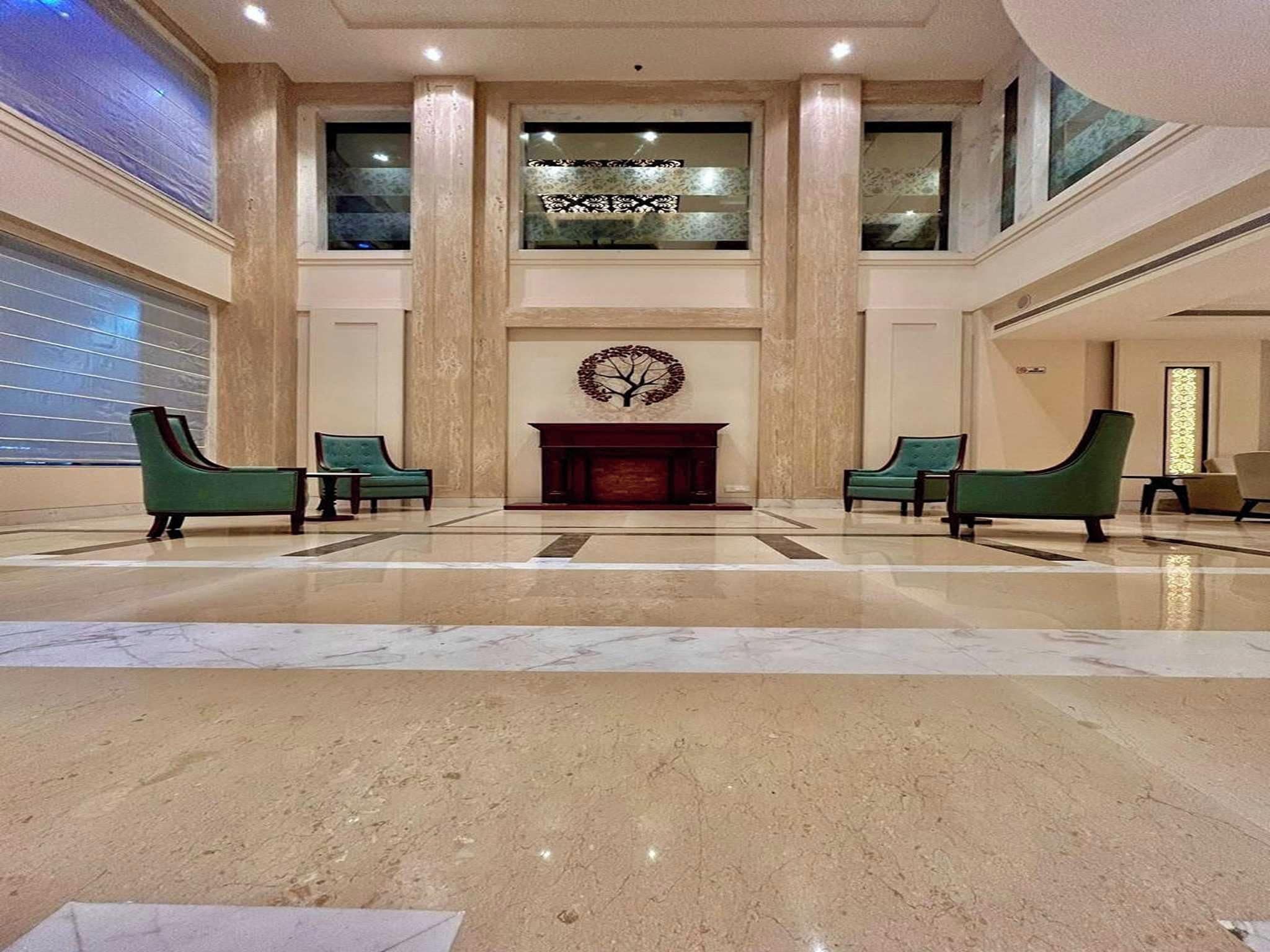 A spacious lobby with a marble floor, two green armchairs, a fireplace, and a decorative wall piece.
