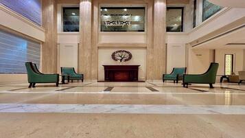 A spacious lobby with a marble floor, two green armchairs, a fireplace, and a decorative wall piece.