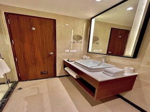 Une salle de bain moderne avec une porte en bois, un grand miroir, un lavabo blanc et un porte-serviettes.
