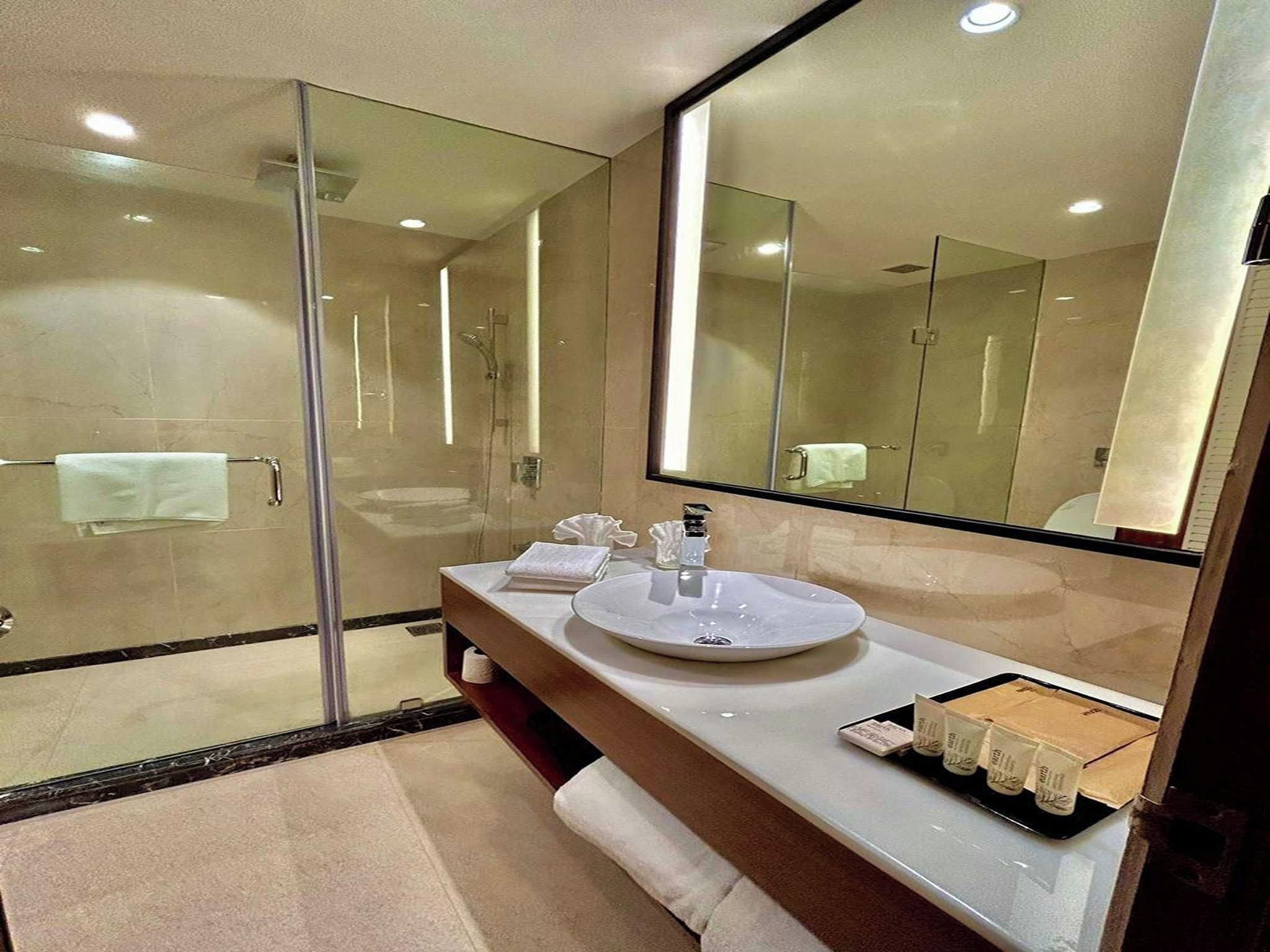 Un baño moderno con cabina de ducha de vidrio, un lavabo redondo y un espejo grande.