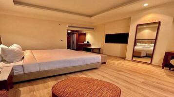 A hotel room with a bed, a desk, a chair, a mirror, and a small ottoman.