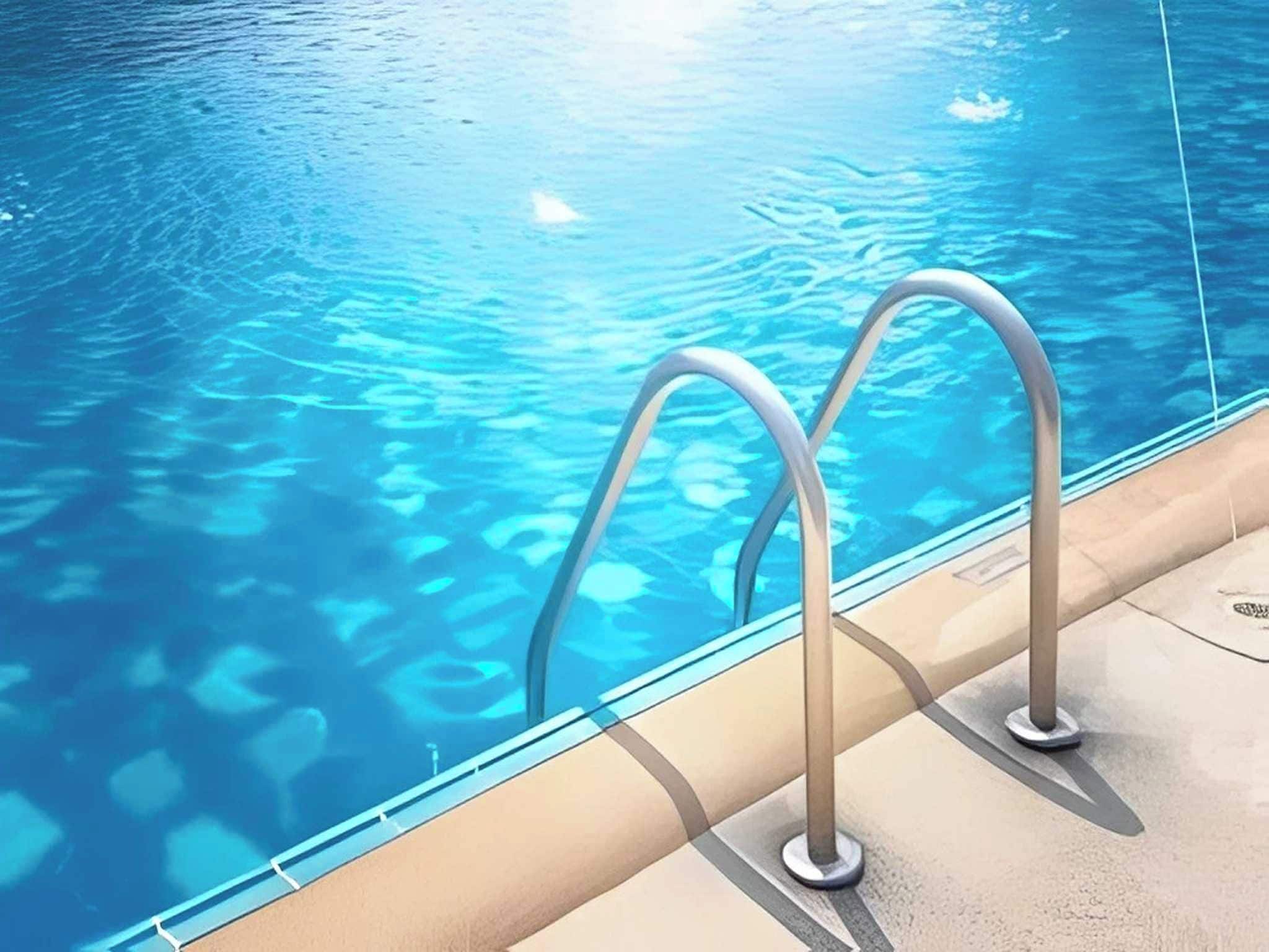 A swimming pool with clear water and metal pool ladders on the edge.