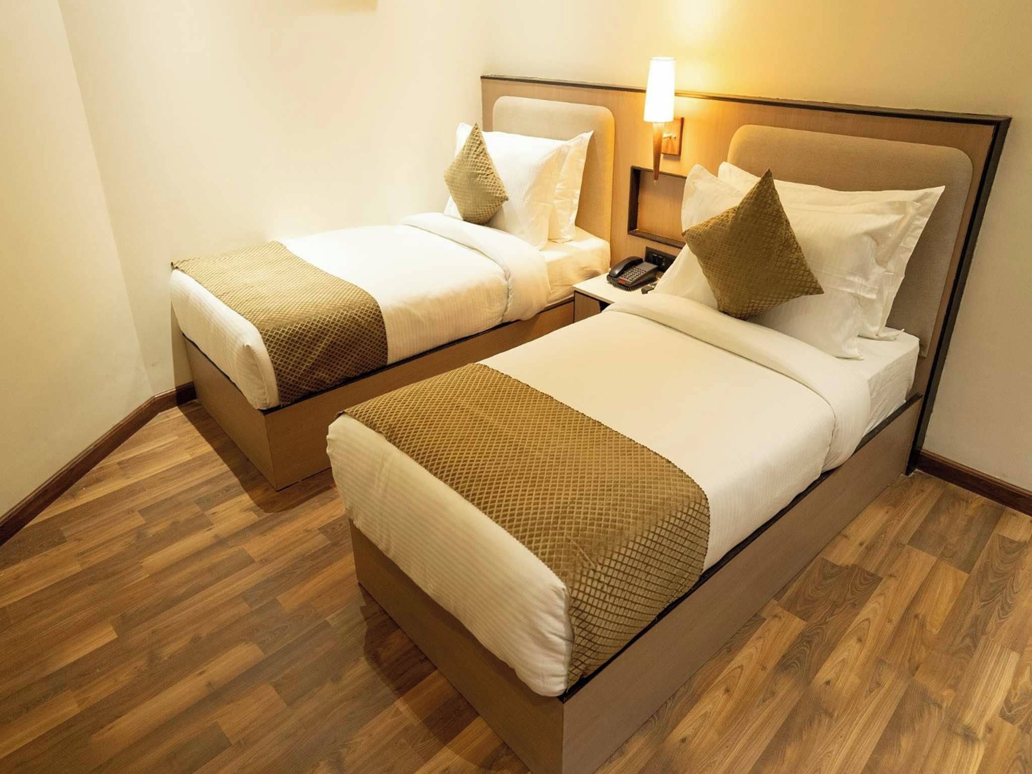 A hotel room with two beds, each with a headboard, pillows, and a bedside table with a phone.