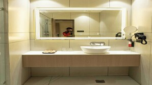 Une salle de bain moderne avec un grand miroir, un lavabo blanc et un petit miroir fixé au mur.