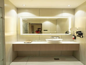 Une salle de bain moderne avec un grand miroir, un lavabo blanc et un petit miroir fixé au mur.