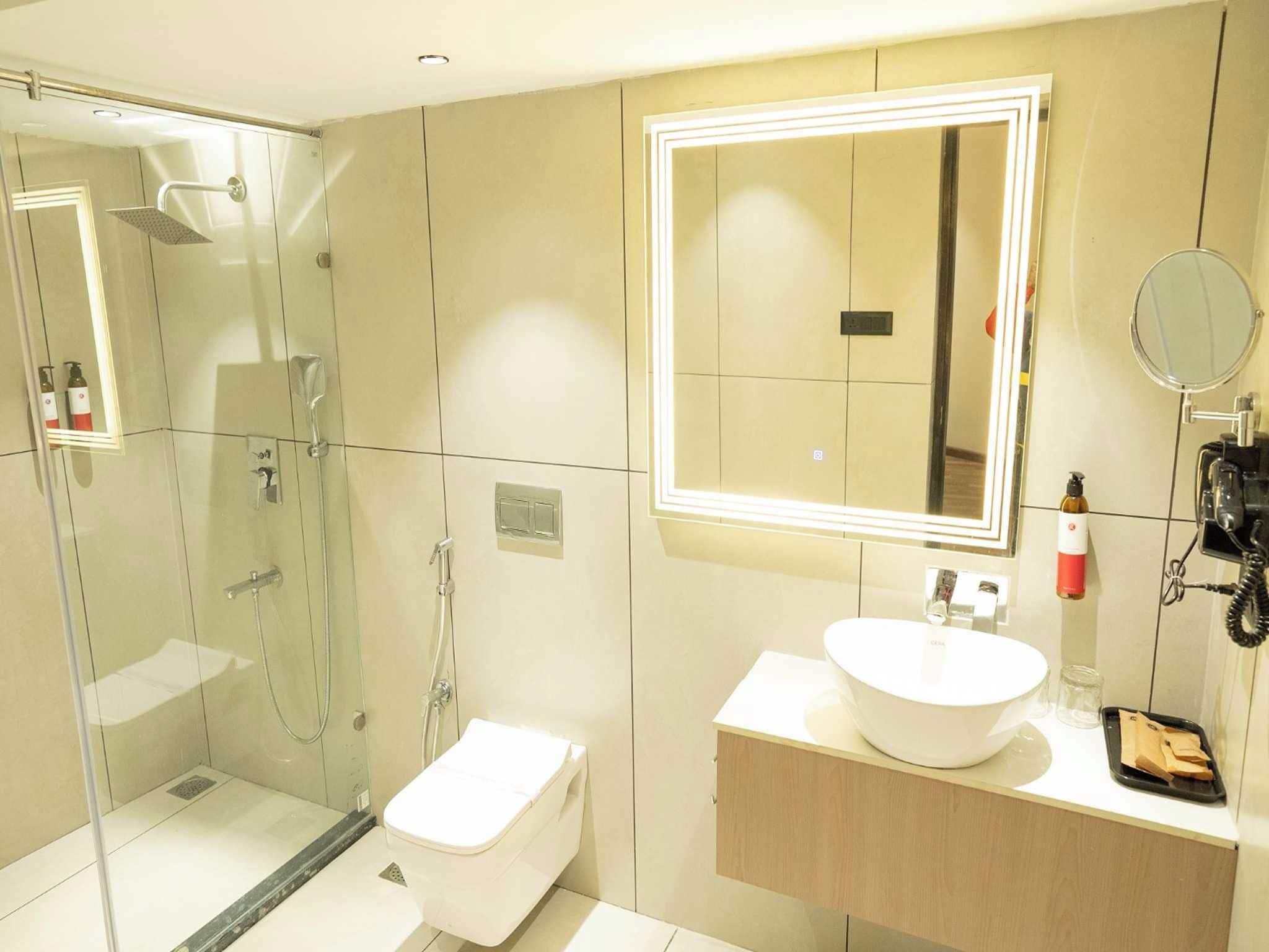 Un baño moderno con ducha envuelta en vidrio, un lavamanos blanco y un espejo con iluminación integrada.