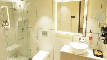 Un baño moderno con ducha envuelta en vidrio, un lavamanos blanco y un espejo con iluminación integrada.