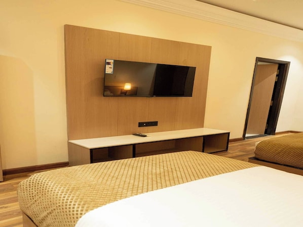 A hotel room with a bed, a TV mounted on the wall, a bedside table, and a door. - Palette Hotel by CheckIn Amritsar City (Amritsar)