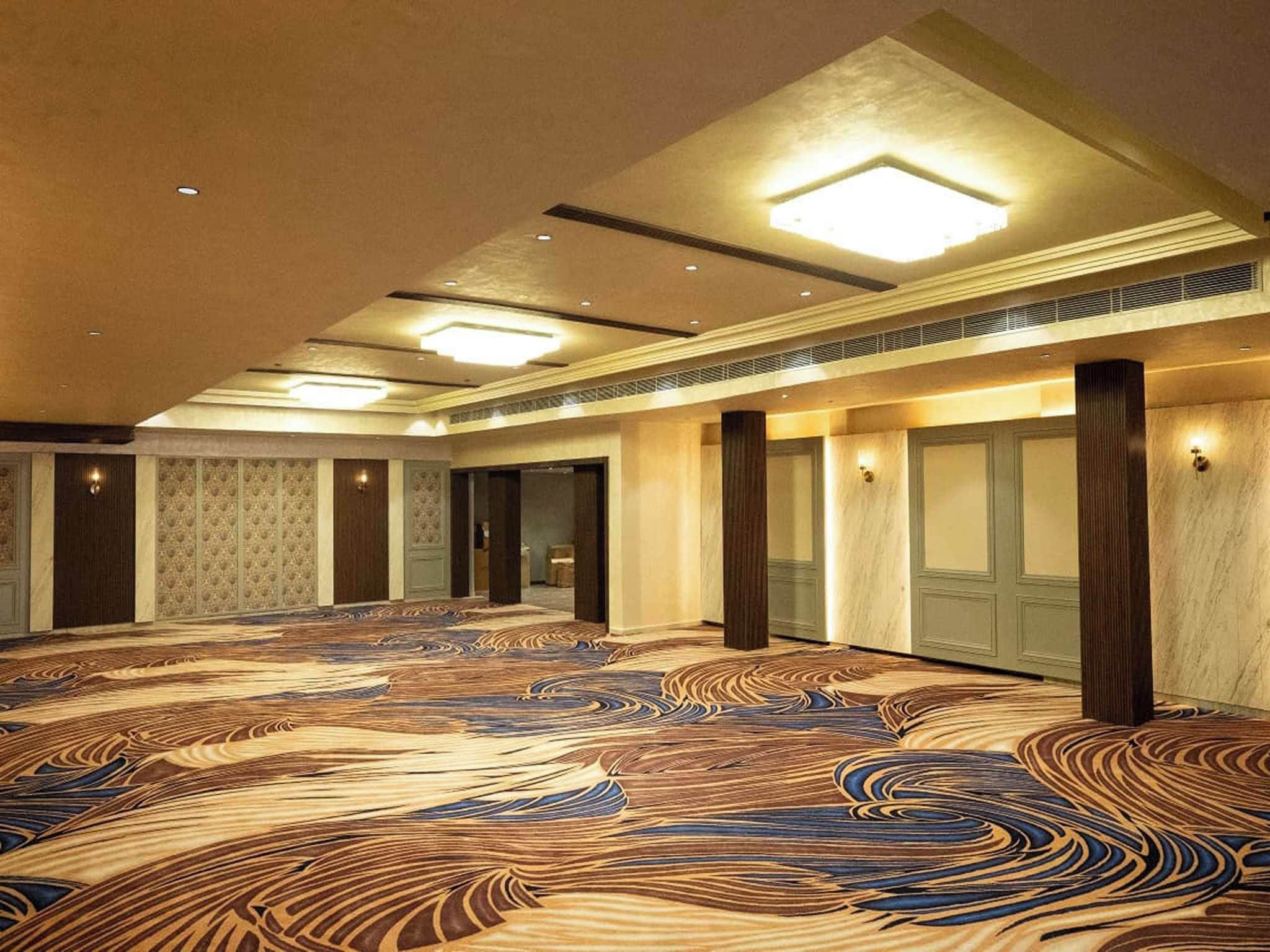 A spacious hall with a patterned carpet, recessed lighting, and a symmetrical layout with columns.