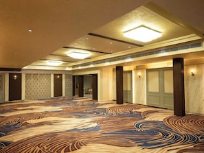 Un hallo espacioso con alfombra estampada, iluminación empotrada y una distribución simétrica con columnas.