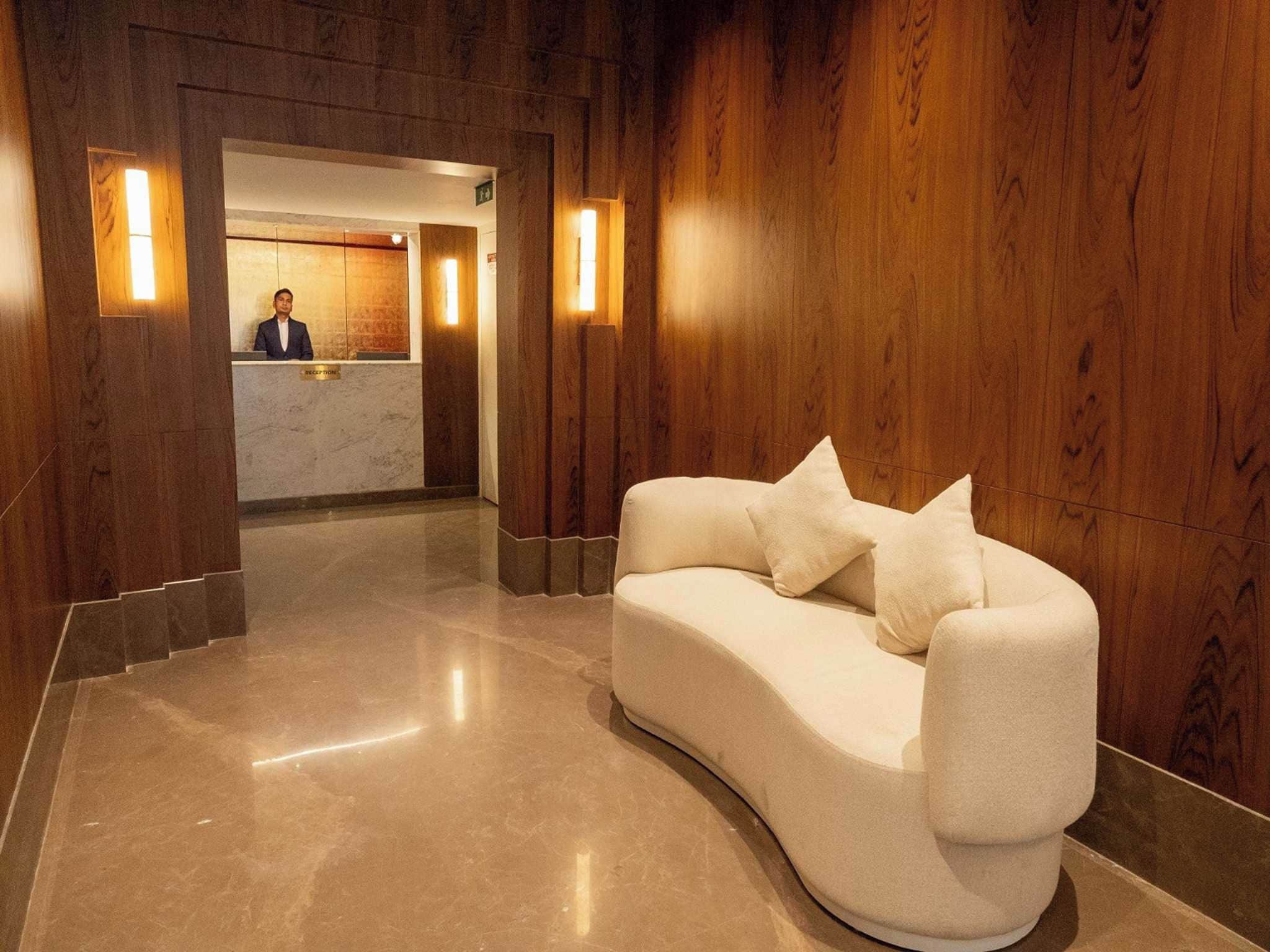 A reception area with a receptionist desk, a curved white sofa with cushions, and wooden paneling on the walls.