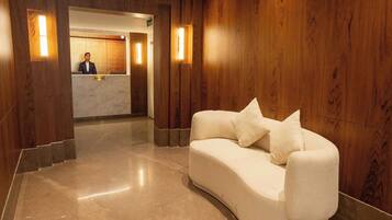 A reception area with a receptionist desk, a curved white sofa with cushions, and wooden paneling on the walls.