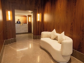 Un área de recepción con mostrador, un sofá blanco curvo con cojines y paneles de madera en las paredes.