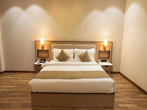 Une chambre d’hôtel avec un grand lit, deux tables de chevet et des lampes fixées au mur.