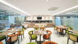 A modern dining area with multiple tables and chairs, a central kitchen counter, and a television mounted on the wall. - Palette Hotel by CheckIn, Visakhapatnam (Visakhapatnam)