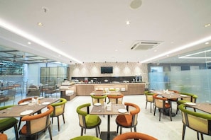 A modern dining area with multiple tables and chairs, a central kitchen counter, and a television mounted on the wall. - Palette Hotel by CheckIn, Visakhapatnam (Visakhapatnam)