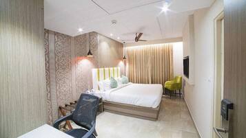 Habitación de hotel con cama, escritorio, silla, televisor y ventilador de techo.