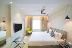 Una habitación de hotel con cama, televisor, ventilador de techo y ventana con cortinas.