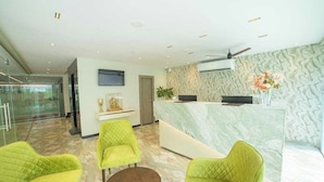 A reception area with a marble counter, green upholstered chairs, a small table, and a television. - Palette Hotel by CheckIn, Visakhapatnam (Visakhapatnam)