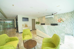 A reception area with a marble counter, green upholstered chairs, a small table, and a television. - Palette Hotel by CheckIn, Visakhapatnam (Visakhapatnam)