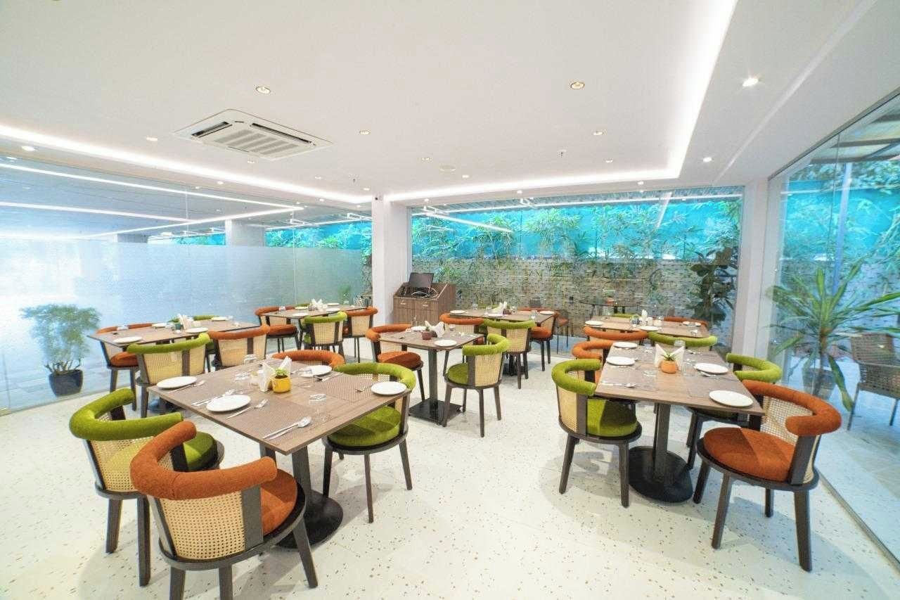A restaurant with multiple tables and chairs, a large window with a view of greenery, and a modern ceiling design.