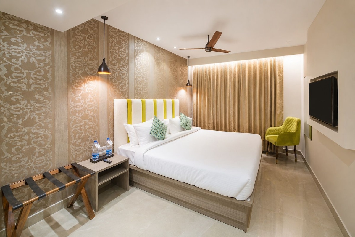A hotel room with a bed, bedside table, chair, and a TV mounted on the wall.