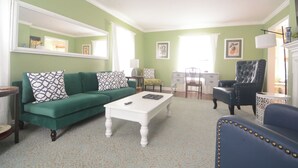 A living room with a green sofa, a white coffee table, a blue armchair, and a fireplace. - first floor, 5 Min to Ball State & Hospital, great fire pit, deck ,full kitchen (Muncie)