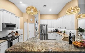 A modern kitchen with white cabinets, stainless steel appliances, and a granite countertop. - Delightful 4-bedroom house with AC  & Heated Pool in sunny Cape Coral (Cape Coral)