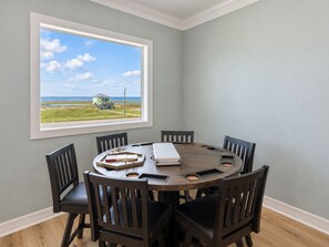 A dining area with a round table and six chairs, a window with a view of a grassy field and a structure, and a white ceiling. - Beachfront, Private Elevator, Hot Tub, Sleeps 24 (Freeport)