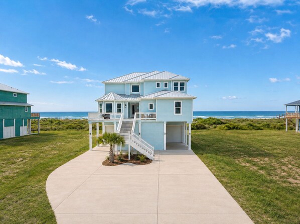 A two-story beachfront house with a covered porch, a staircase leading to the entrance, and a clear view of the ocean. - Beachfront, Private Elevator, Hot Tub, Sleeps 24 (Freeport)
