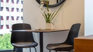 A dining area with a round mirror, two chairs, a table, and a potted plant. - Honeycomb (Auckland)