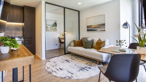 A modern living room with a sofa, coffee table, and a dining area. There is a kitchen visible in the background. - Honeycomb (Auckland)