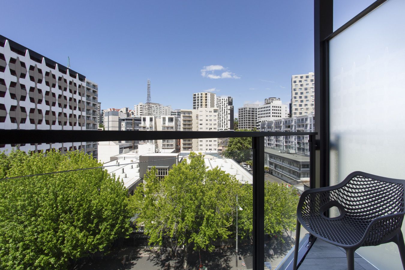 Ein Balkon mit Blick auf eine Stadtansicht, ein Metallstuhl und ein Gebäude mit einer markanten Fassade.