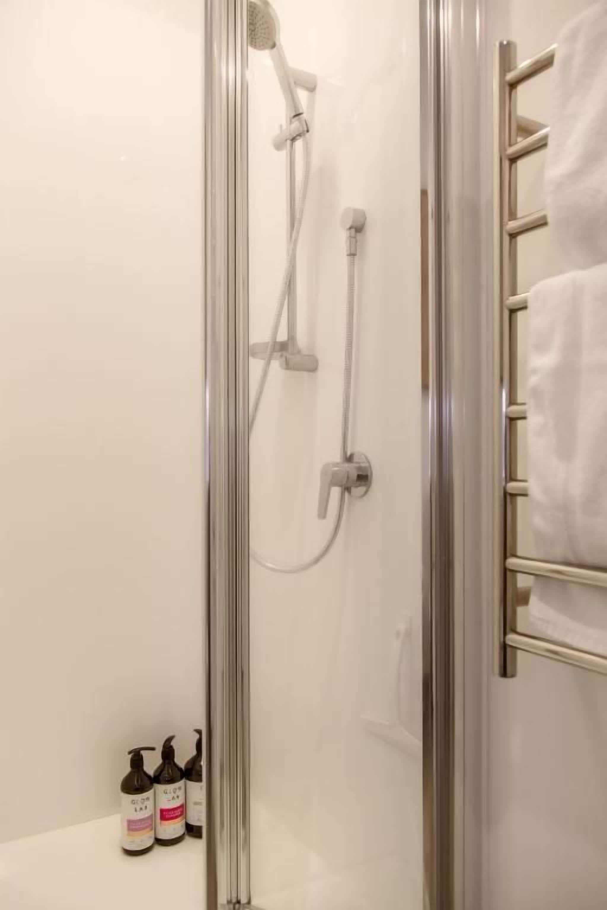 Área de duche envidraçada com um porta-toalhas e duas garrafas de champô.