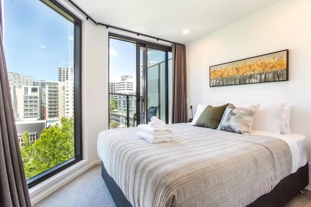 Quarto de hotel com uma janela grande, uma cama com colcha listrada e um quadro na parede.