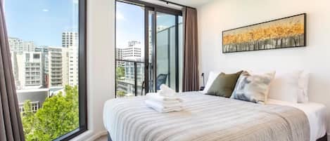 A hotel room with a large window, a bed with a striped bedspread, and a painting on the wall.